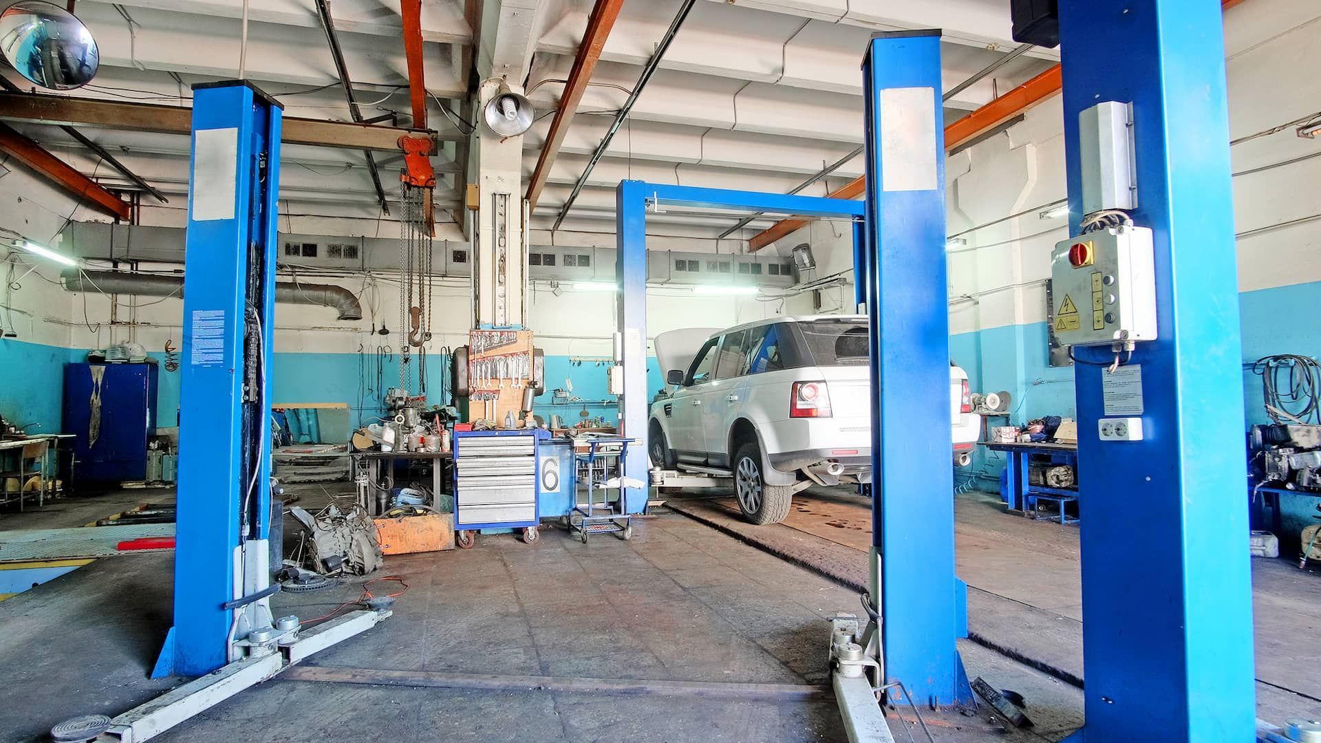 Pont élévateur bleu dans un garage ; une voiture blanche est soulevée.