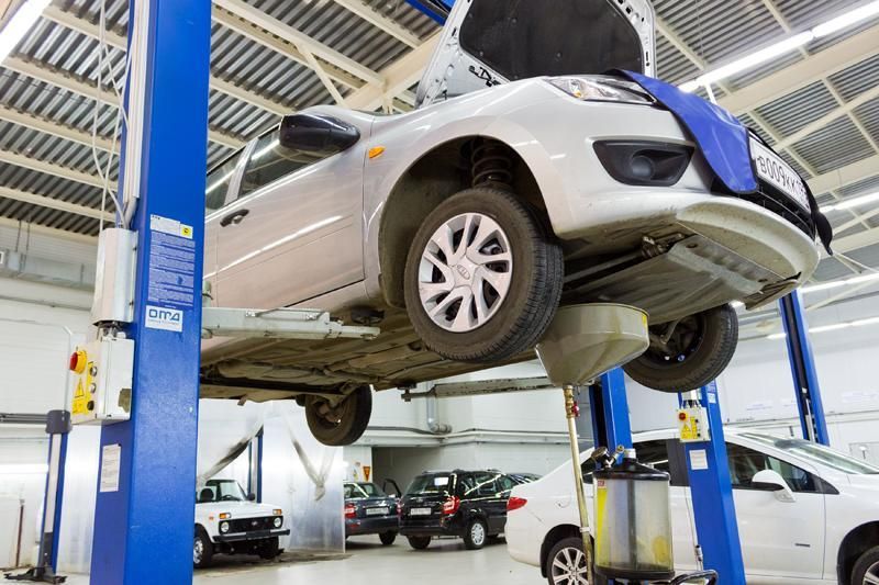 Voiture sur un pont élévateur dans un atelier de réparation ; l'huile s'écoule dans un bac.