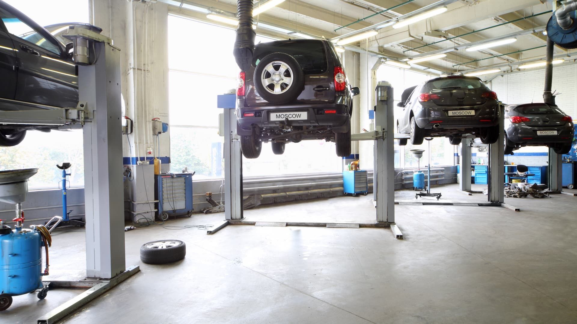 Des voitures sur des ponts élévateurs dans un atelier de réparation automobile bien éclairé ; une voiture a une roue de secours montée.