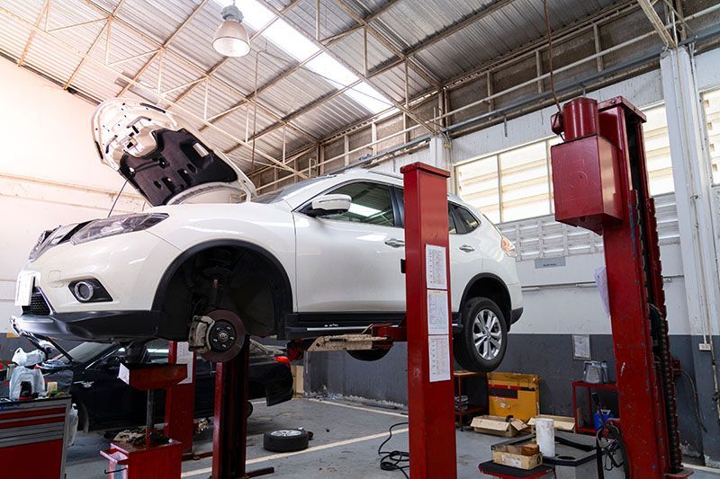 Un SUV blanc, surélevé sur un pont élévateur rouge dans un atelier de réparation, capot ouvert pour entretien.