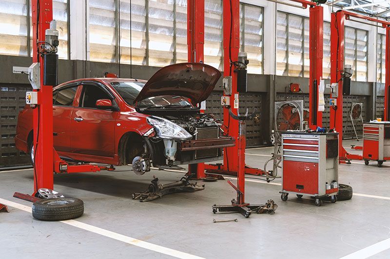 Voiture rouge sur un pont élévateur dans un garage, capot ouvert, outils et équipements.