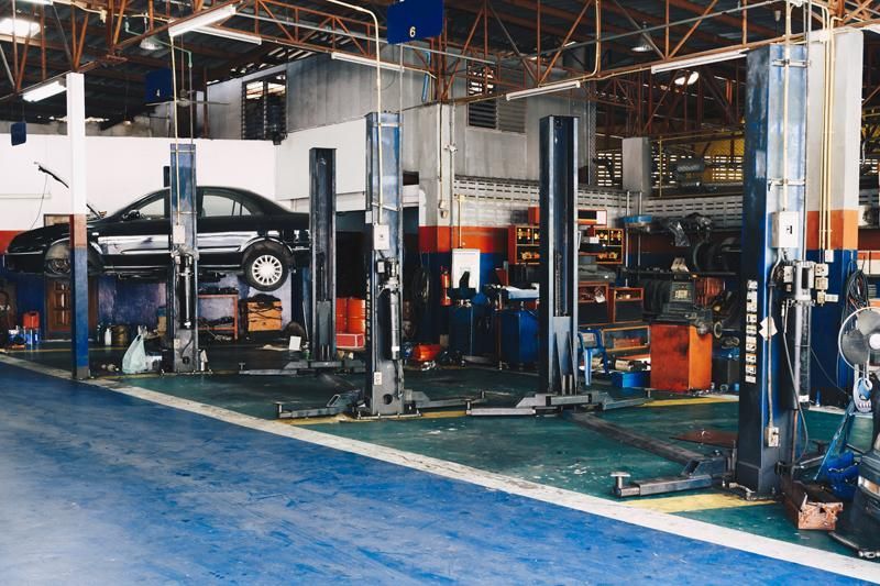 Une voiture en réparation dans un garage, avec plusieurs ponts élévateurs et équipements.