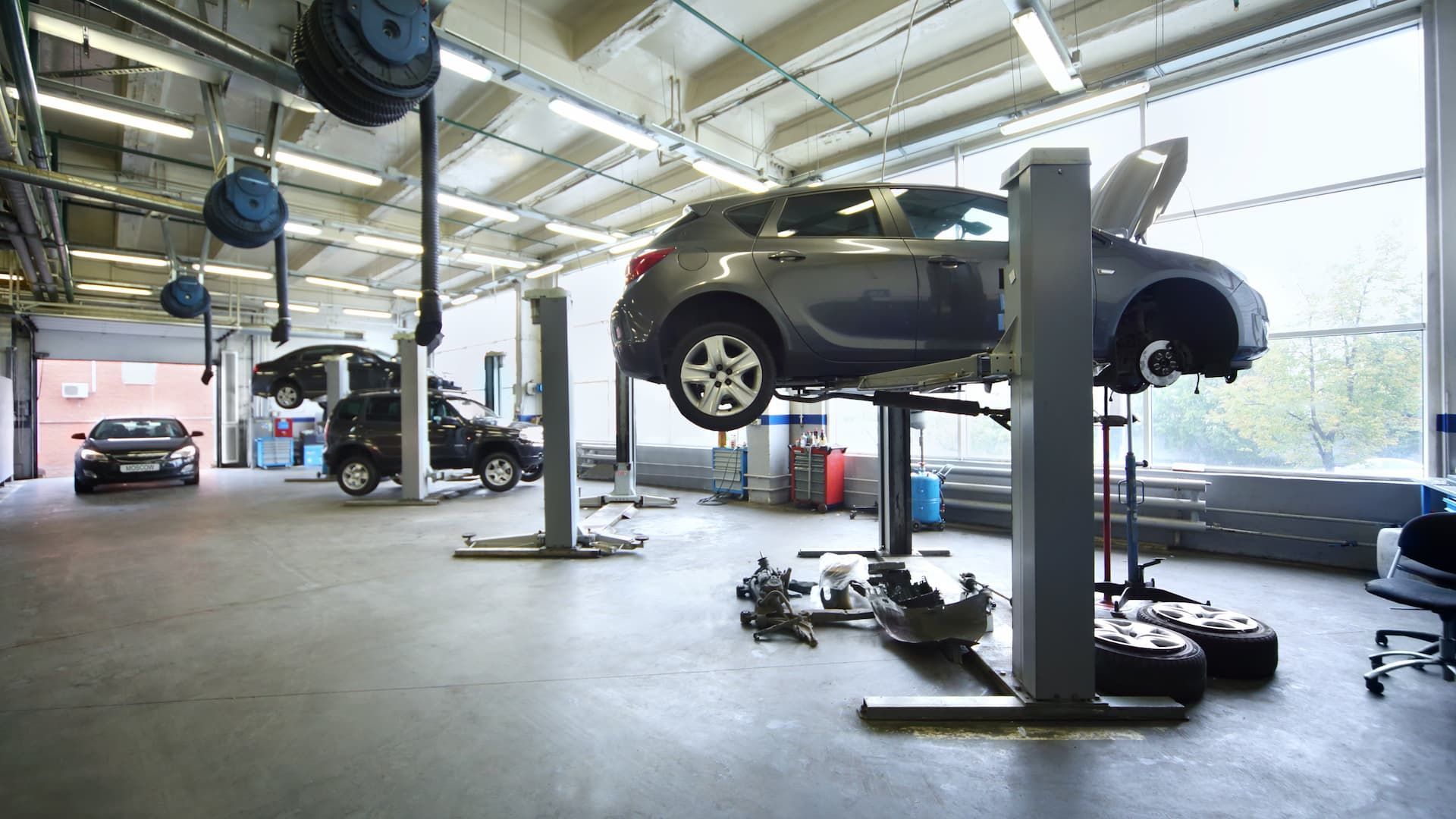Voitures sur des ponts élévateurs dans un garage ; équipements au sol, enrouleurs d'outils fixés au plafond, porte de garage ouverte à l'arrière.