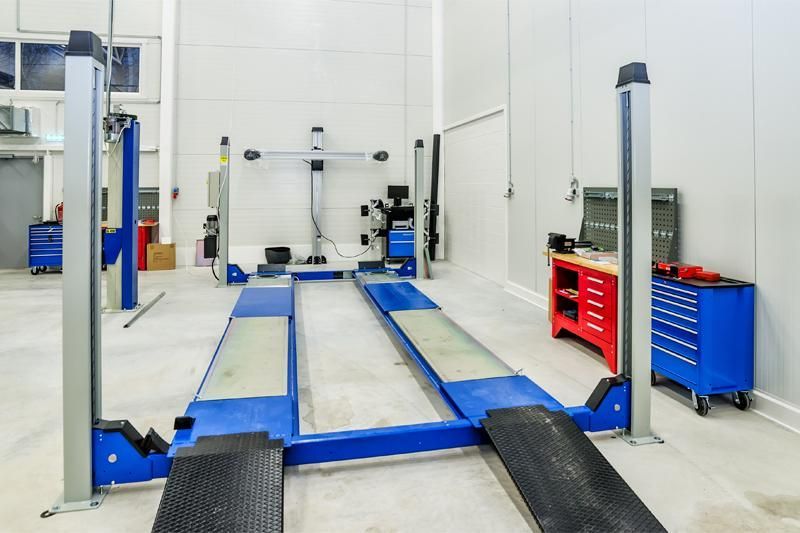 Pont élévateur bleu dans un atelier blanc ; équipement de géométrie, coffres à outils.