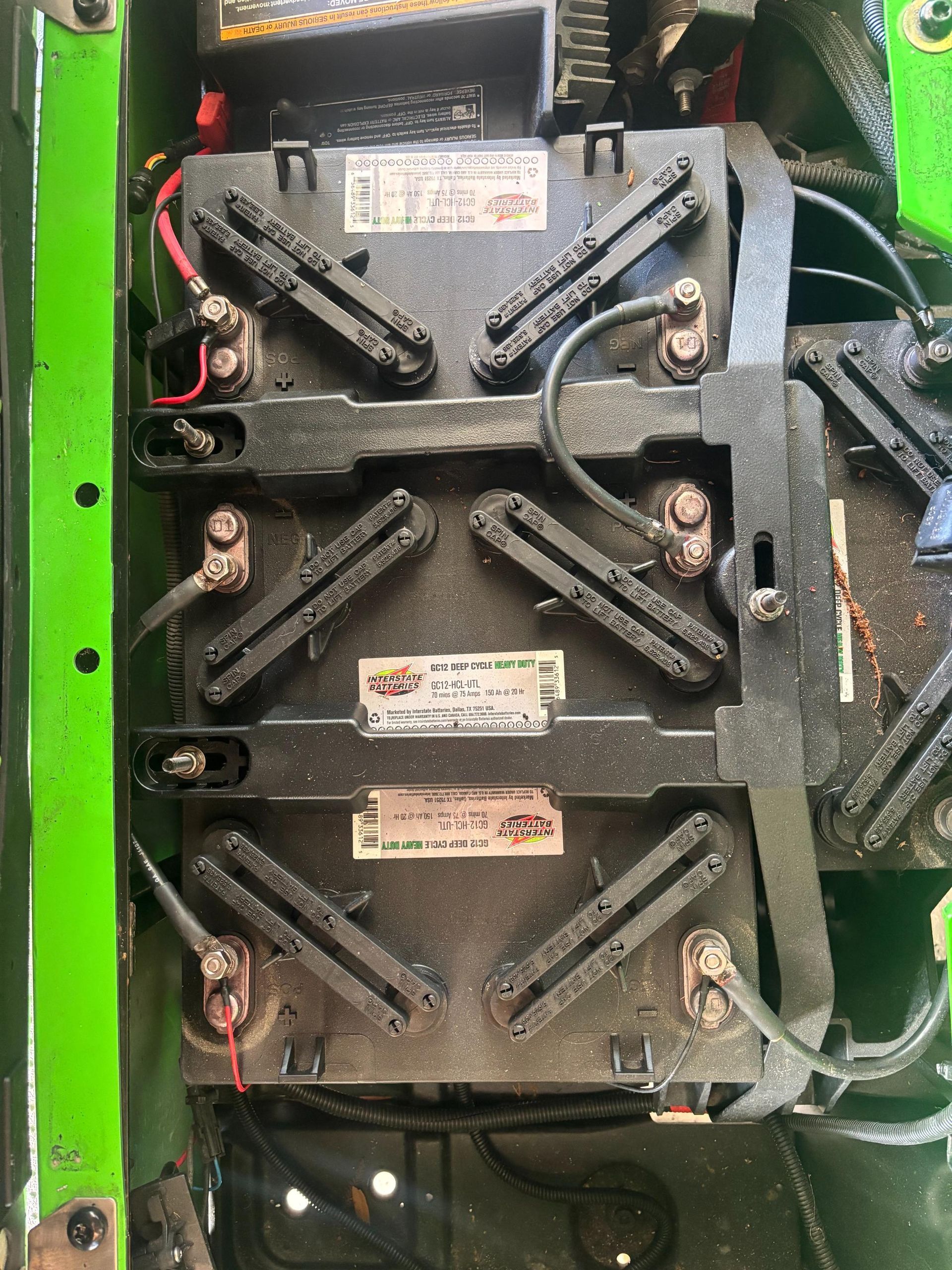Black batteries in a green compartment, connected by wires. Labels are visible on the batteries.