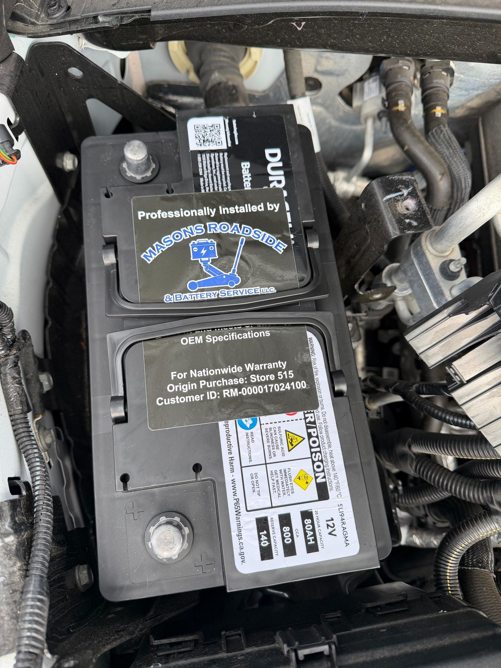 Car battery, black, with instructional stickers, installed in engine compartment.