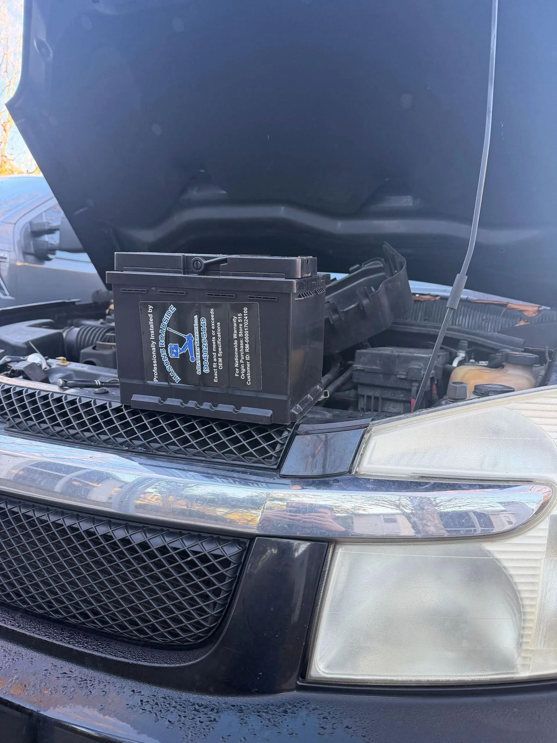 Car battery on top of a car engine under an open hood, showing a vehicle repair.