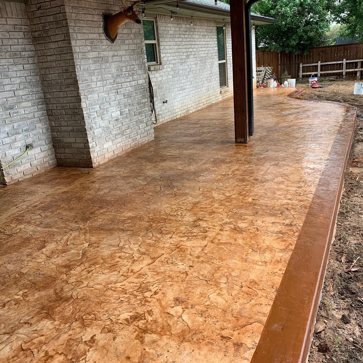 Stamped concrete patio with brown and tan tones next to a white brick wall.