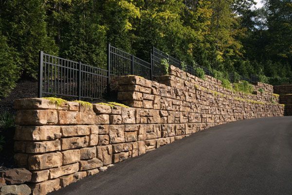 A stone wall along the side of a road next to a fence.