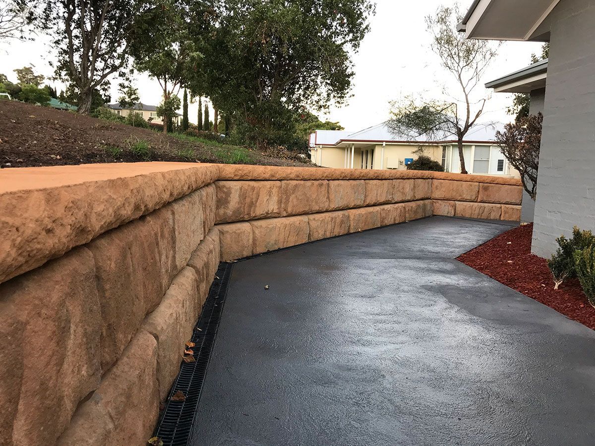 A stone wall along the side of a driveway next to a house.