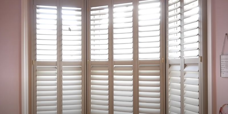 a window with white shutters in a room with a pink wall Customizable plantation shutters Love is Blinds Kentucky (859) 549-3177.