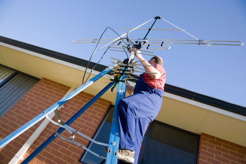 Man On A Ladder Installing A Tv Antenna On A Roof — Aliance Group in Grafton, NSW
