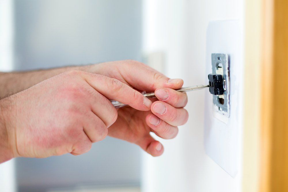 Person Using A Screwdriver To Work On A Light Switch Mounted On A White Wall — Aliance Group in Grafton, NSW