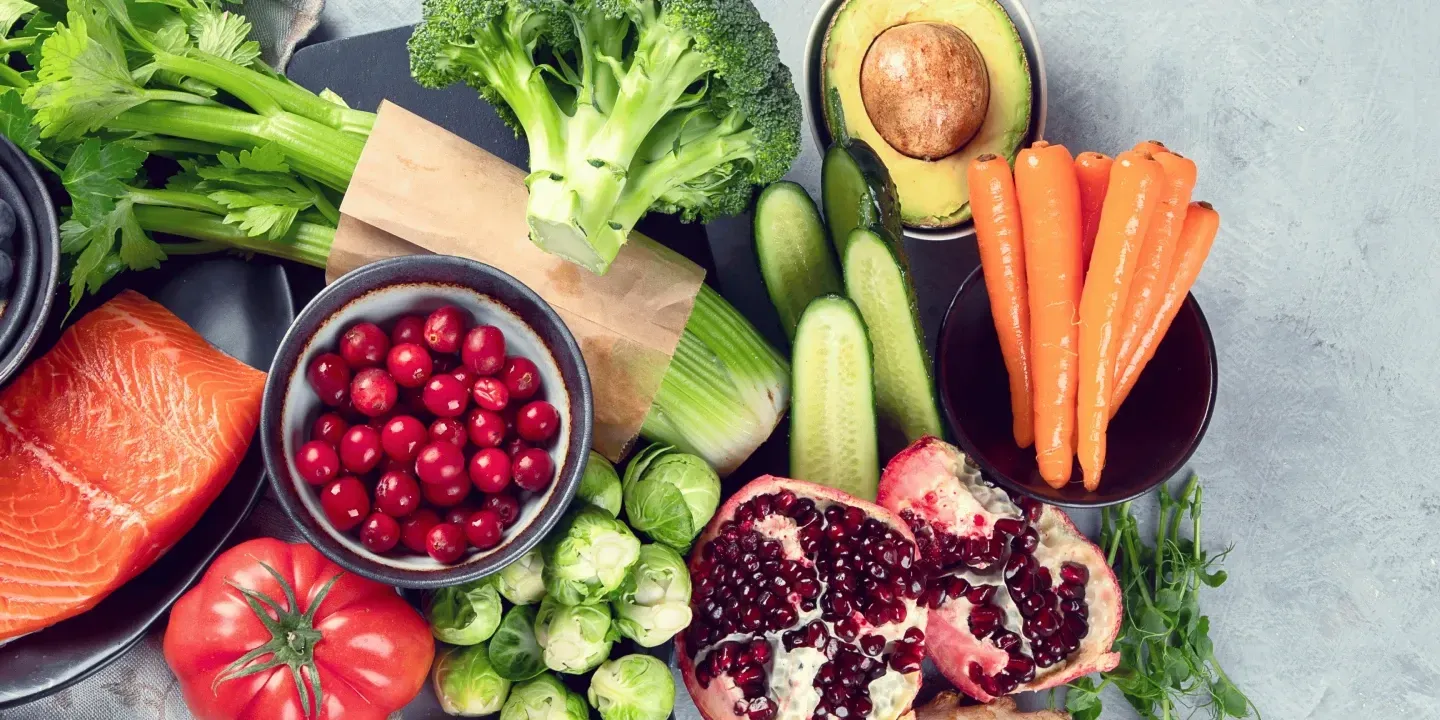 A variety of fresh, colorful fruits and vegetables, including salmon, broccoli, avocado, cranberries, and pomegranate.