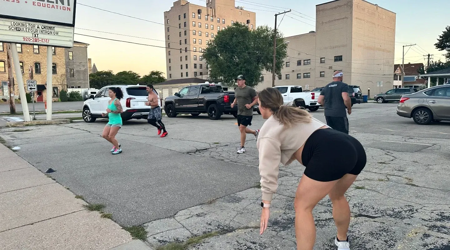 People doing outdoor fitness drills in a parking lot at dusk with apartment buildings nearby