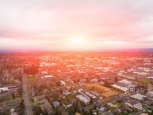An aerial view of a city at sunset with the sun shining through the clouds.