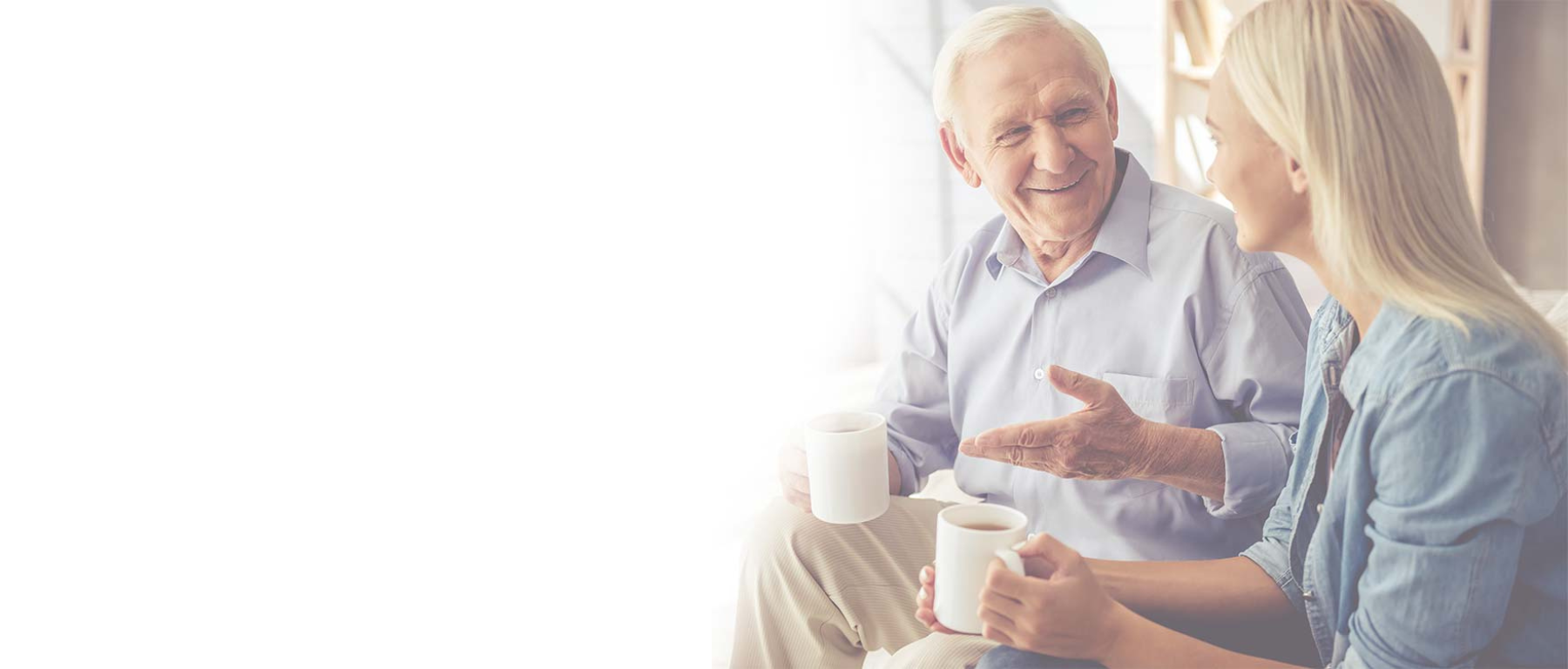 An elderly man and a young woman are sitting next to each other drinking coffee.