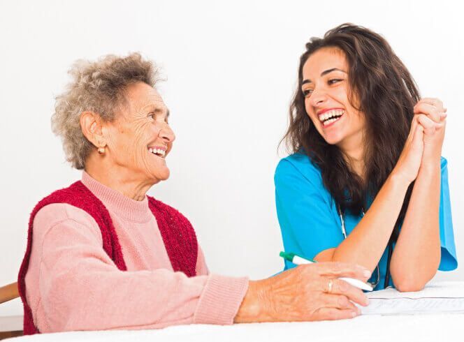 An elderly woman is sitting at a table with a nurse.