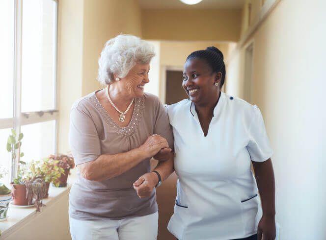 A nurse is helping an elderly woman walk down a hallway.