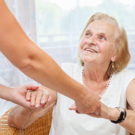 An elderly woman is sitting in a chair holding another woman 's hand.