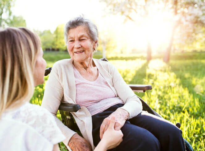 A woman is holding the hand of an elderly woman in a wheelchair.