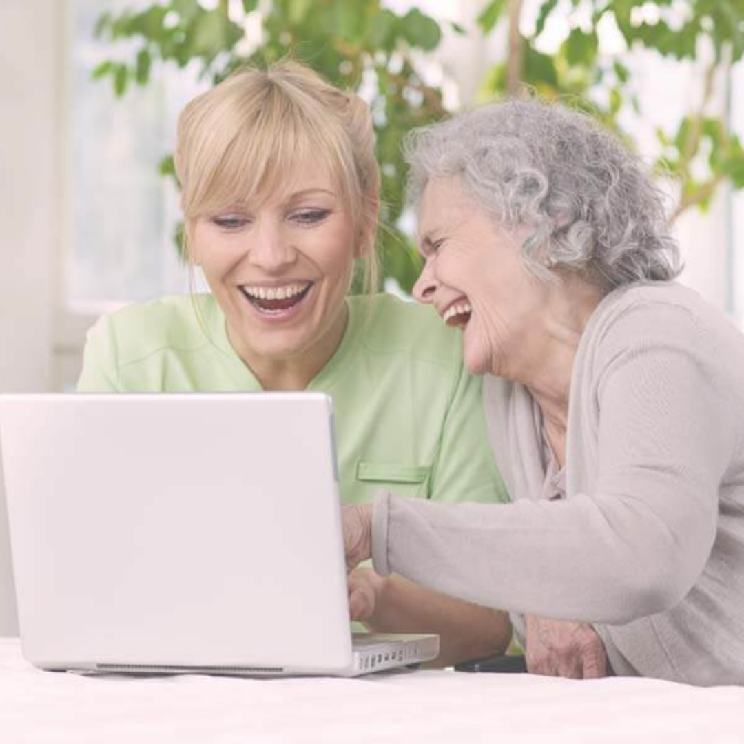 Two women are laughing while looking at a laptop computer