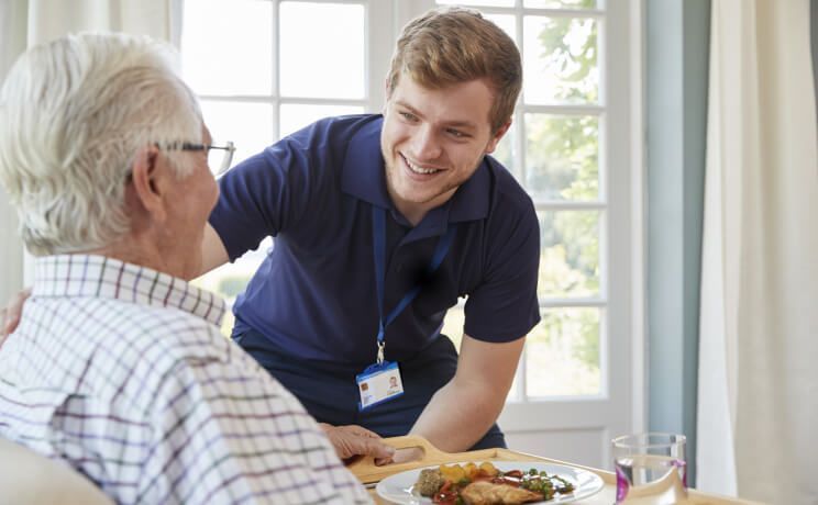 A young man is serving food to an older man at a table.
