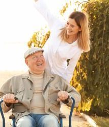 A woman is standing next to an older man in a wheelchair.