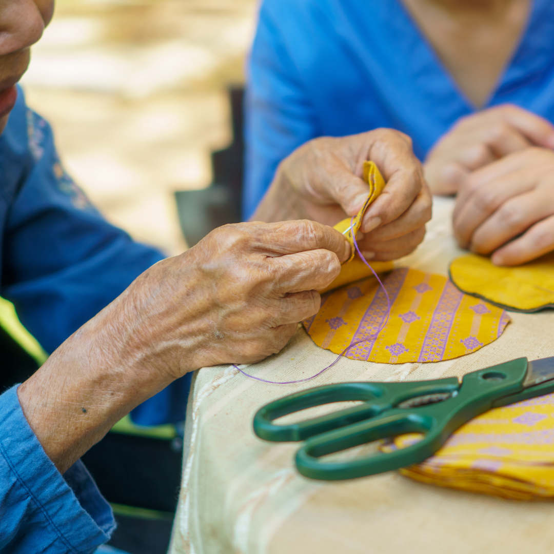 Two people are sitting at a table with scissors and a piece of fabric.