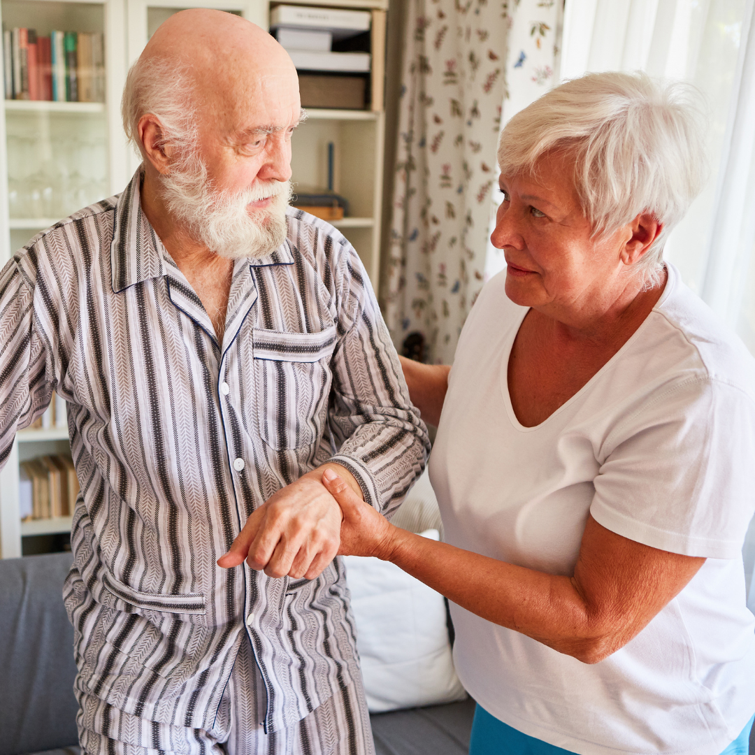 A woman is helping an elderly man walk in a living room