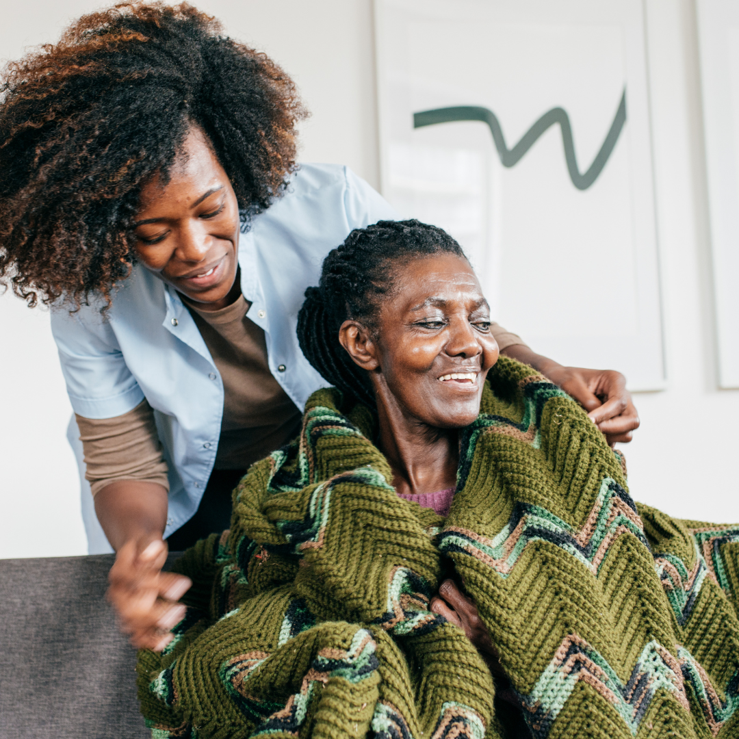 A woman is putting a green blanket on an older woman.