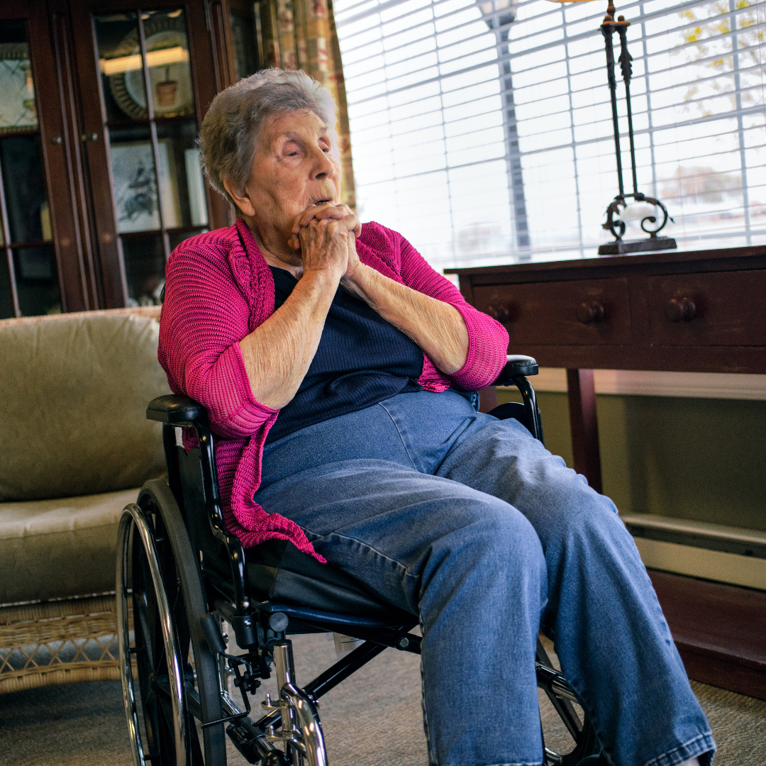 An elderly woman is sitting in a wheelchair in front of a window.