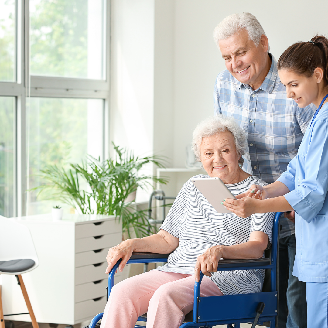 An elderly woman in a wheelchair is looking at a tablet.