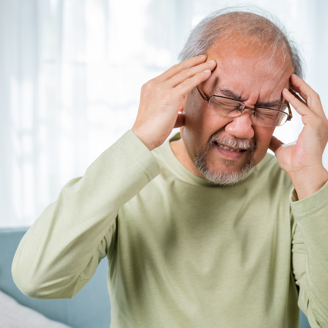 A man wearing glasses is holding his head in pain