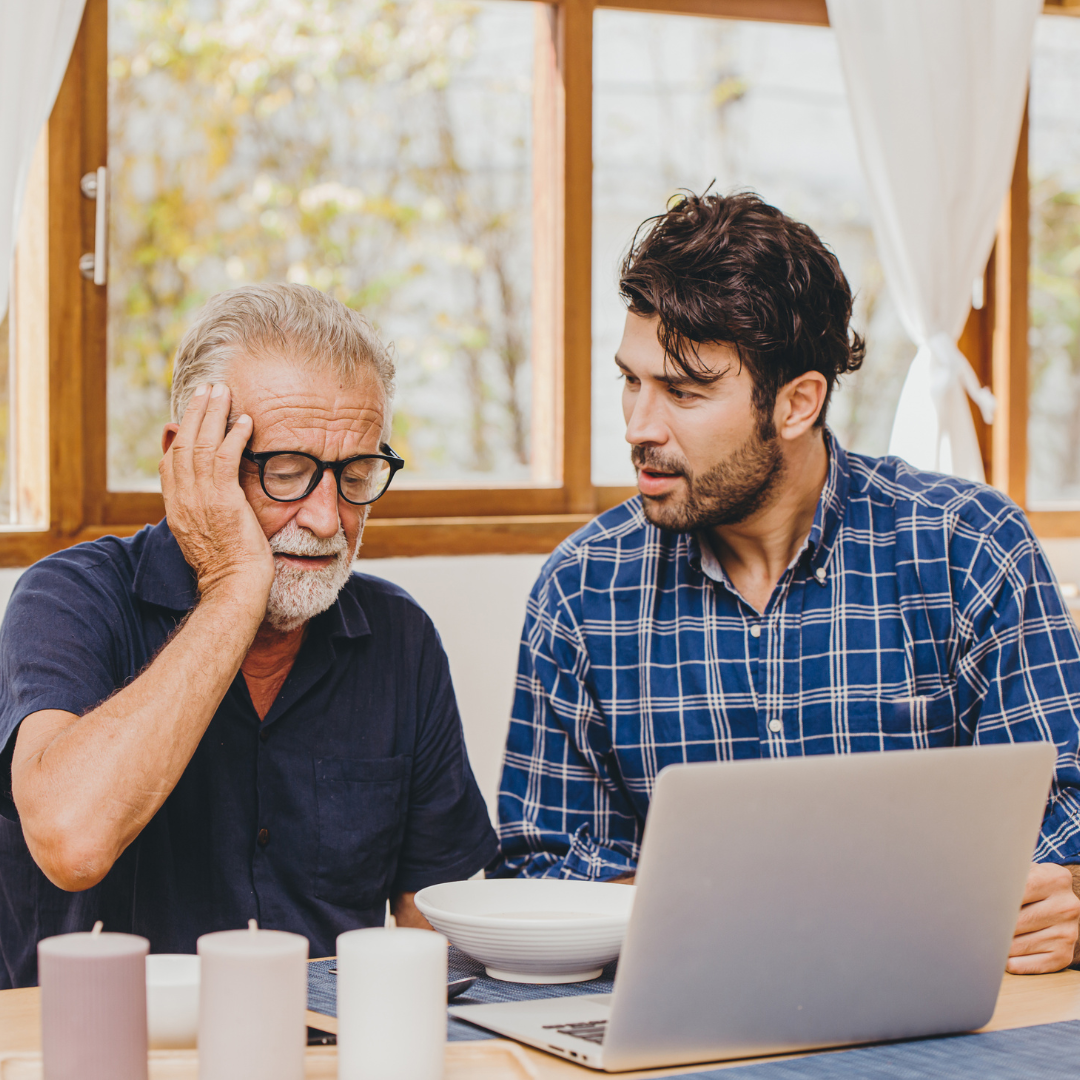 Two men are sitting at a table looking at a laptop computer.