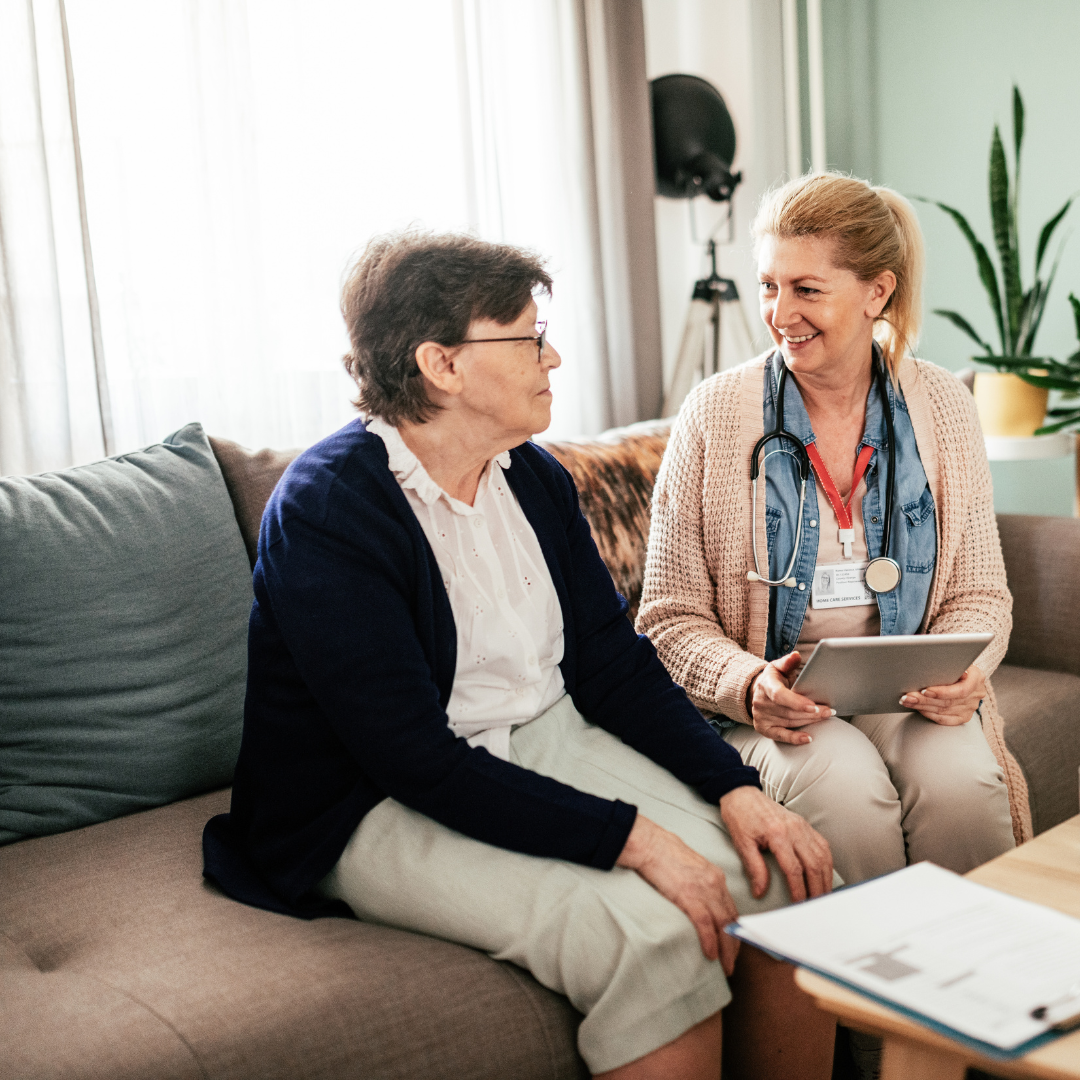Two women are sitting on a couch looking at a tablet.
