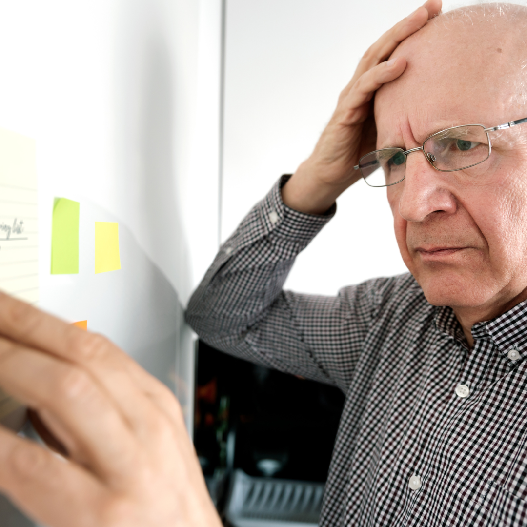 A man wearing glasses and a plaid shirt is writing on a whiteboard