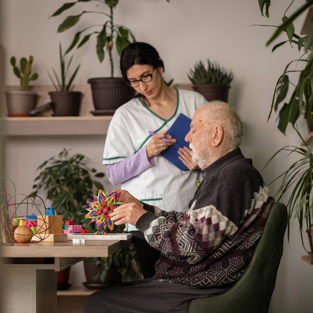 A nurse is talking to an elderly man who is sitting at a table.