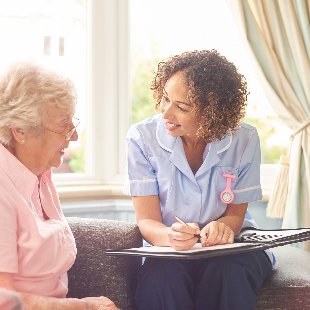 A nurse is talking to an older woman who is sitting on a couch.