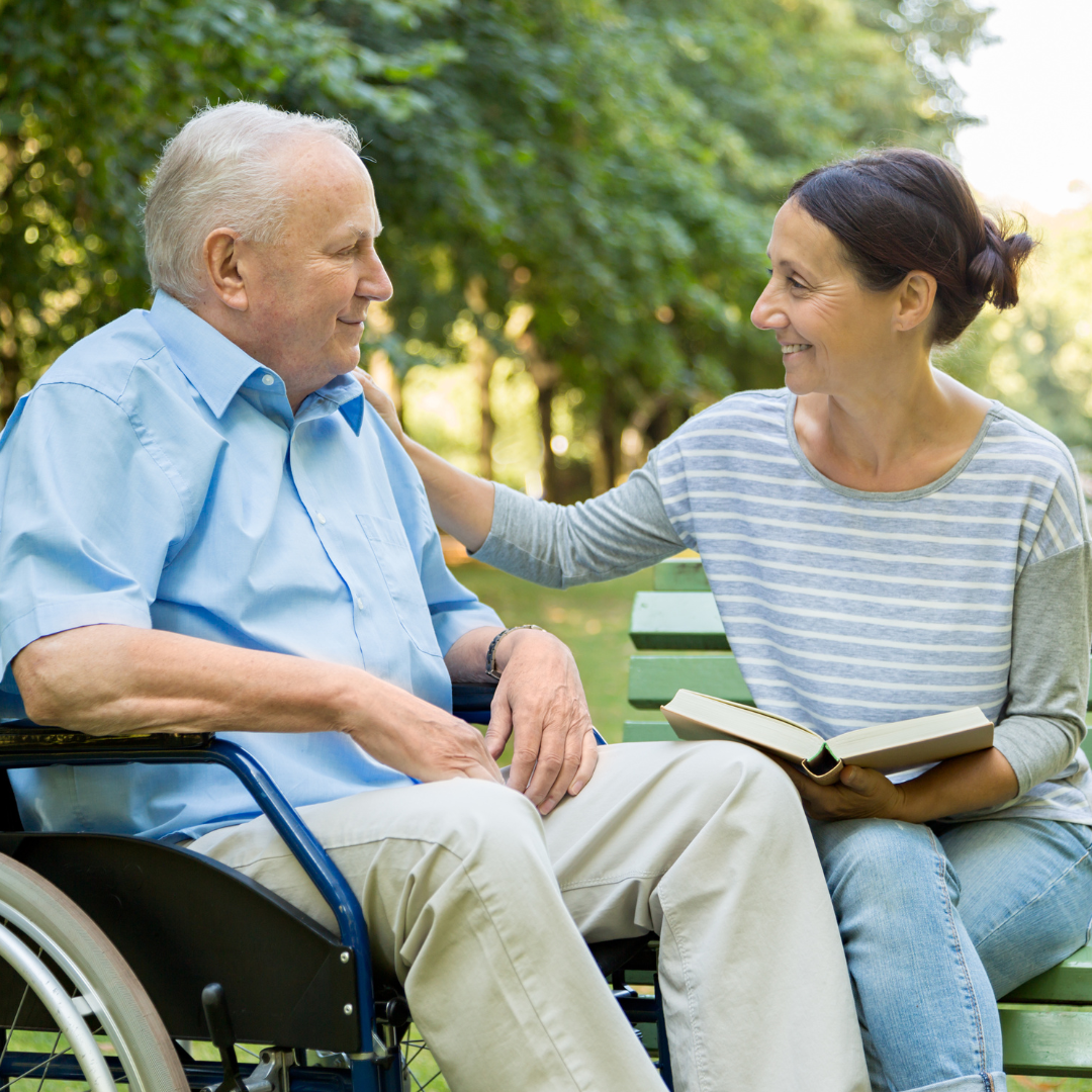 A woman is sitting on a bench next to an older man in a wheelchair.