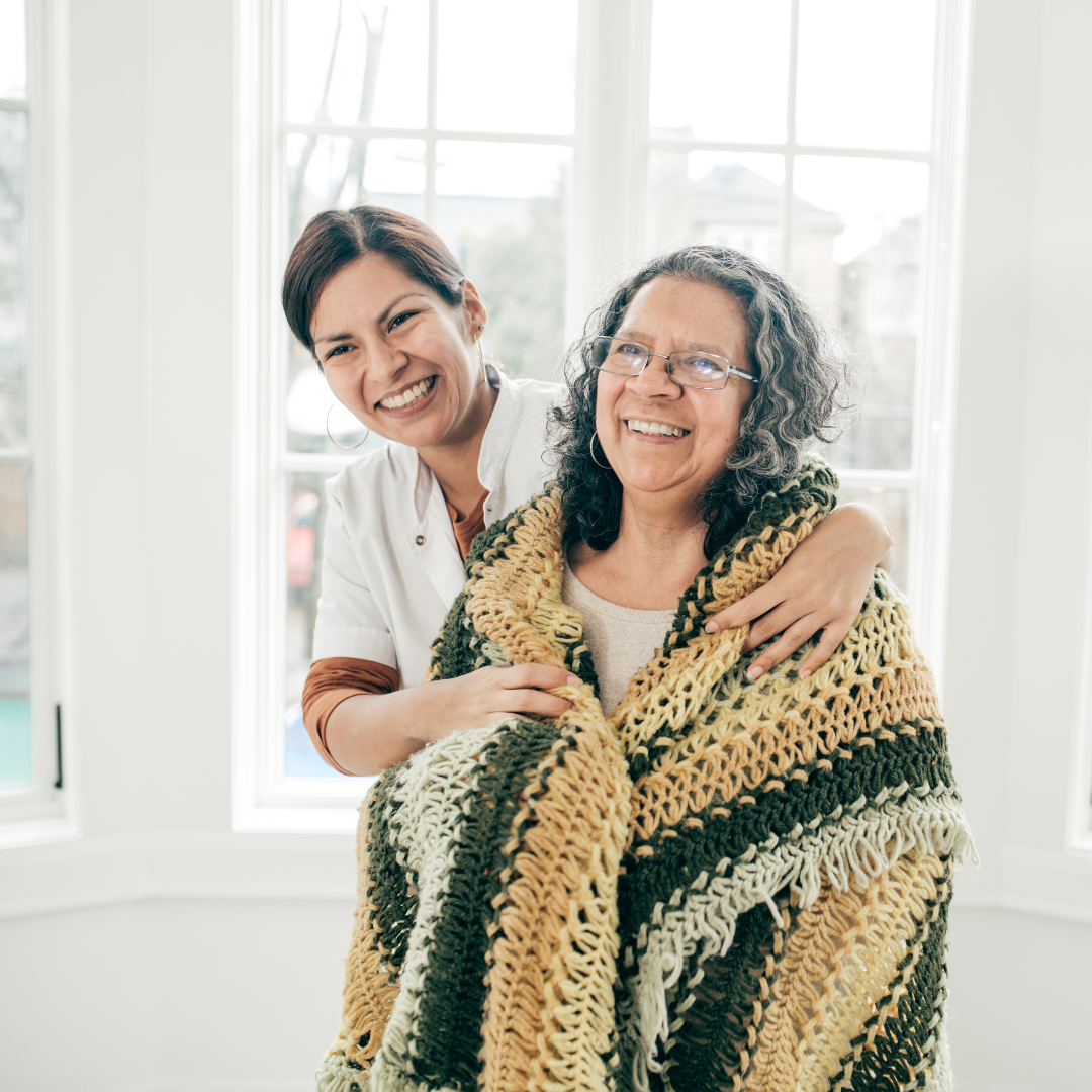 A nurse is hugging an older woman wrapped in a blanket.