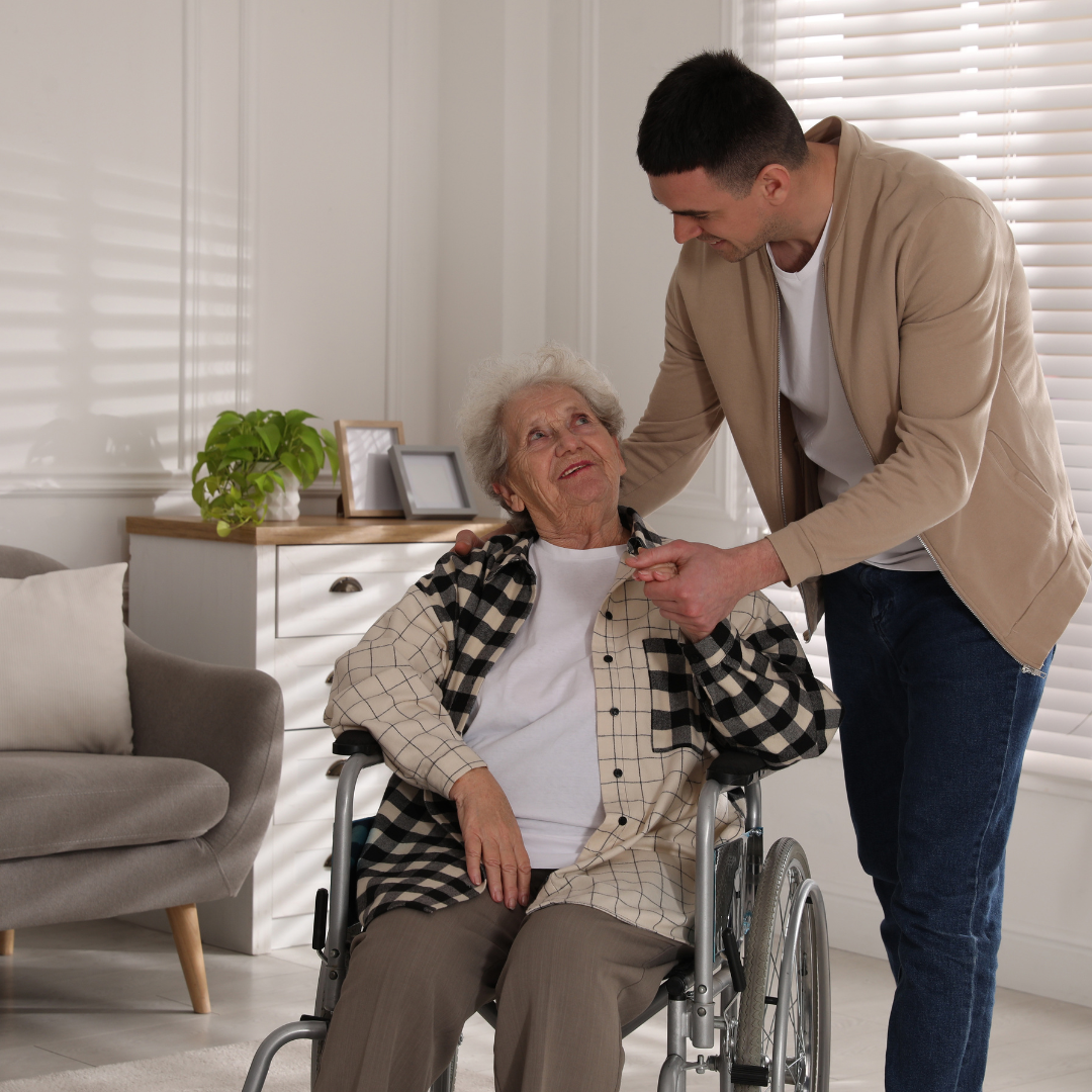A man is standing next to an elderly woman in a wheelchair.