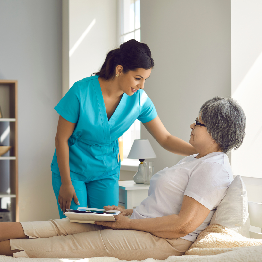 A nurse is talking to an elderly woman laying on a bed.