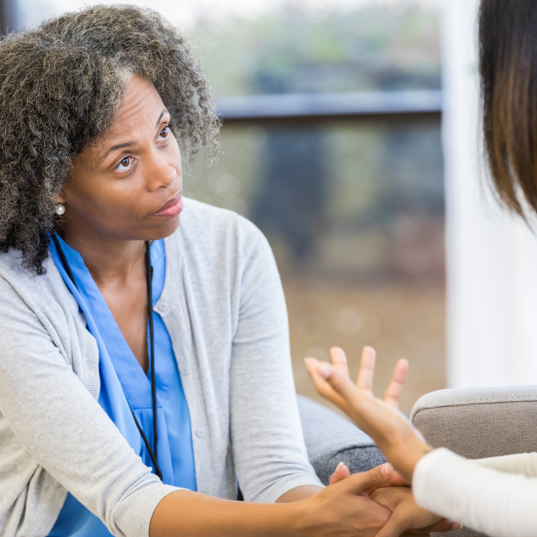 A woman is sitting on a couch talking to another woman.