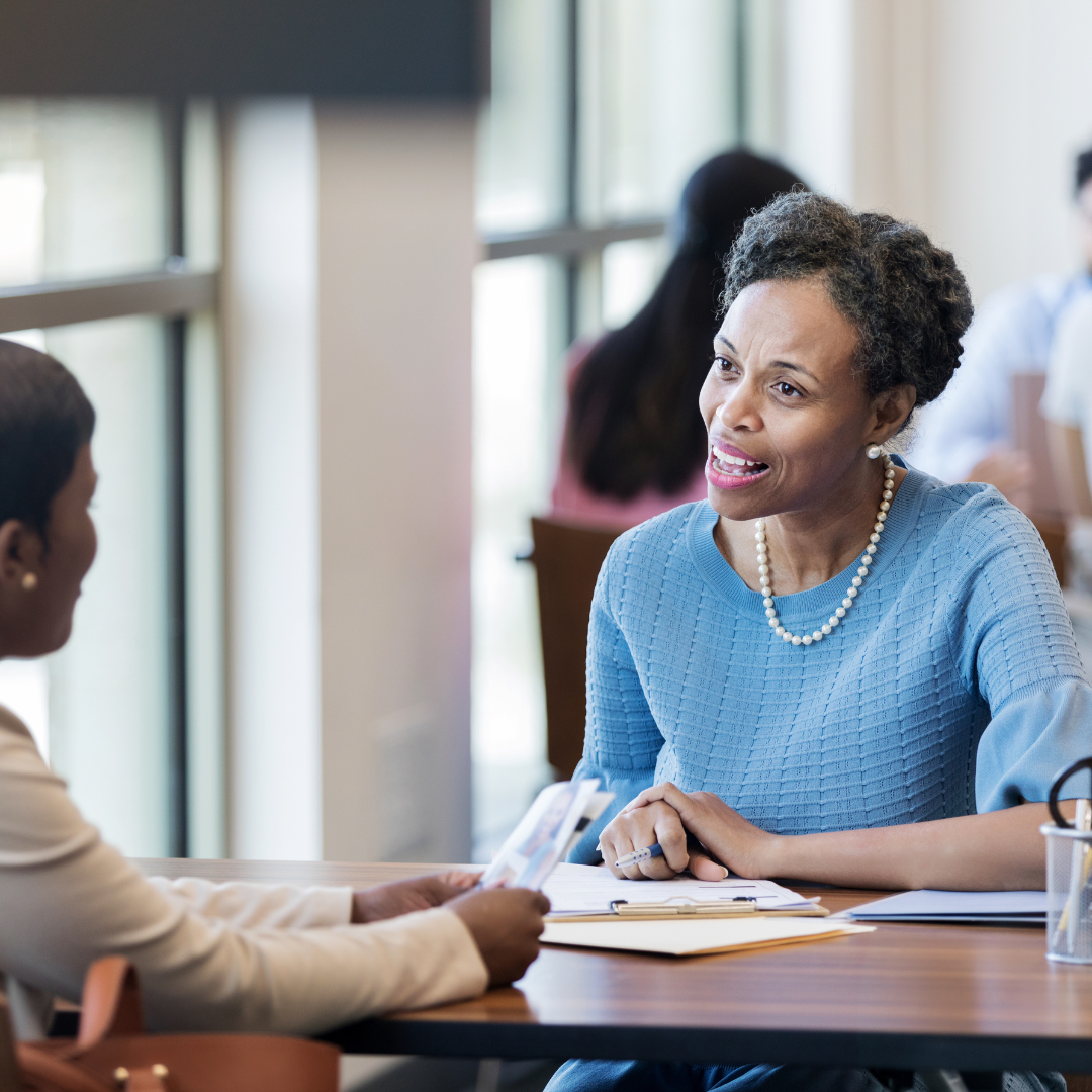 Two women are sitting at a table talking to each other.