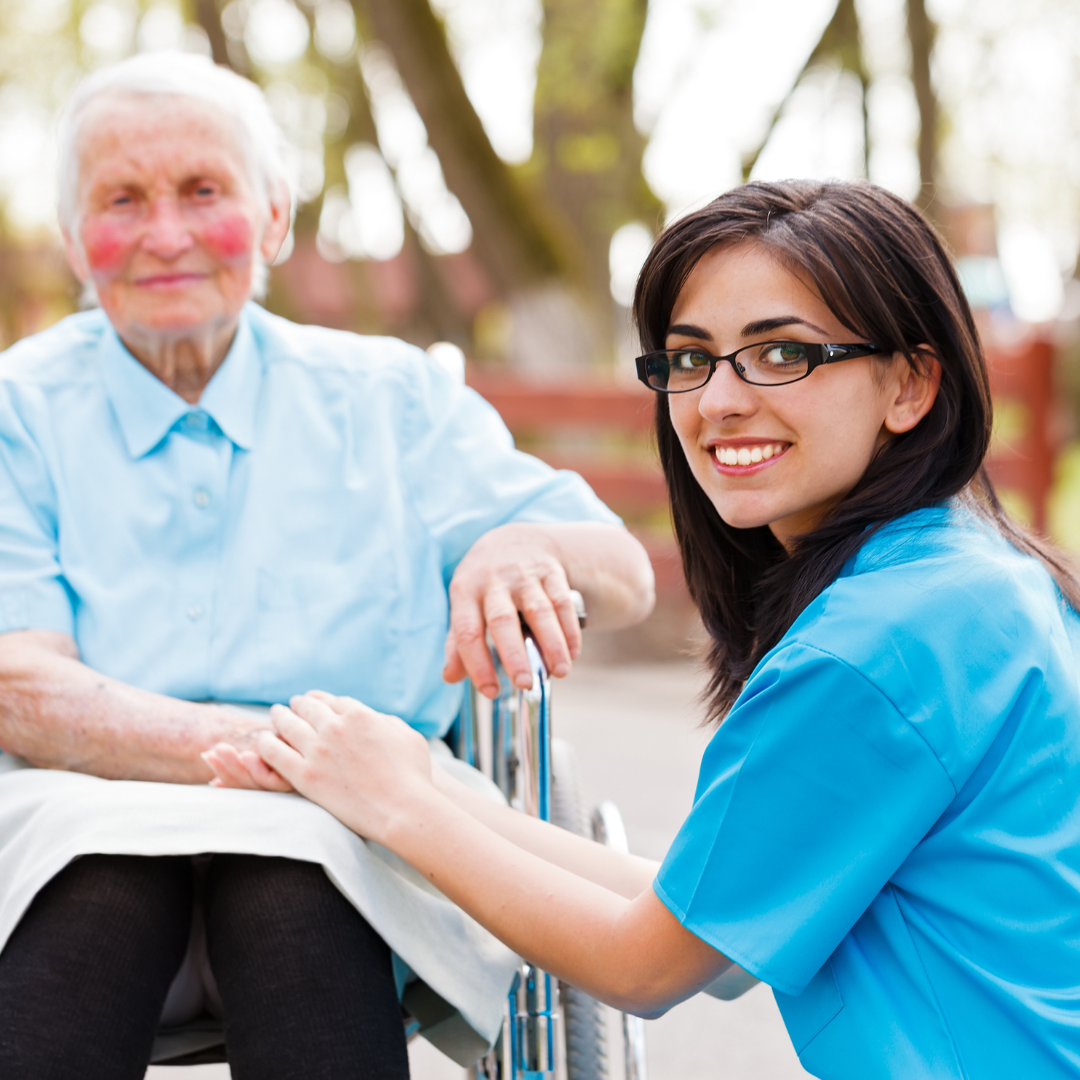 A woman in a blue shirt sits next to an older woman in a wheelchair
