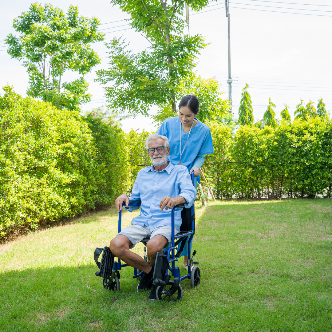 an elderly man's companion pushes him in a wheelchair outside on a sunny day.