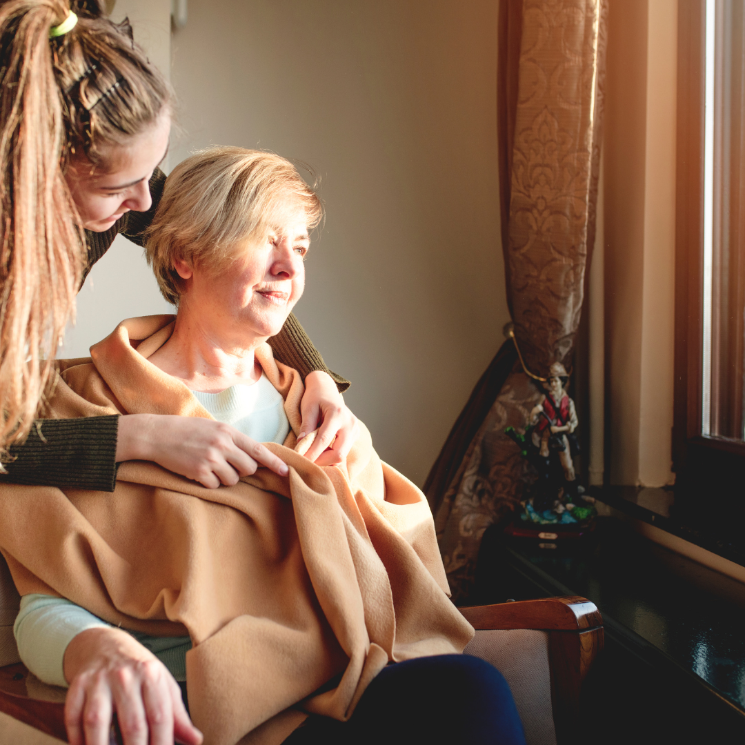 A woman is putting a blanket on an older woman who is sitting in a chair