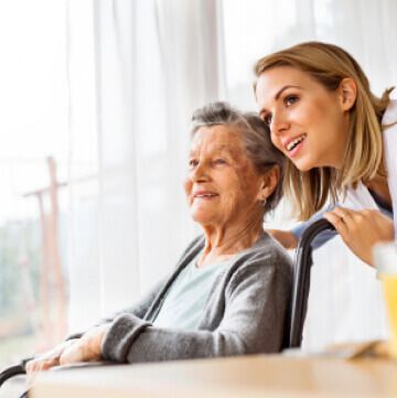 A woman is standing next to an older woman in a wheelchair.