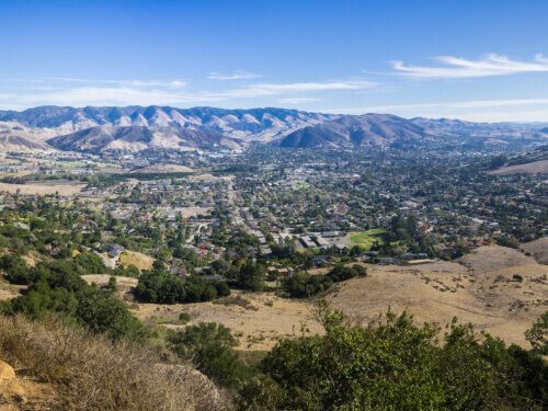 A view of a city from a hill with mountains in the background.